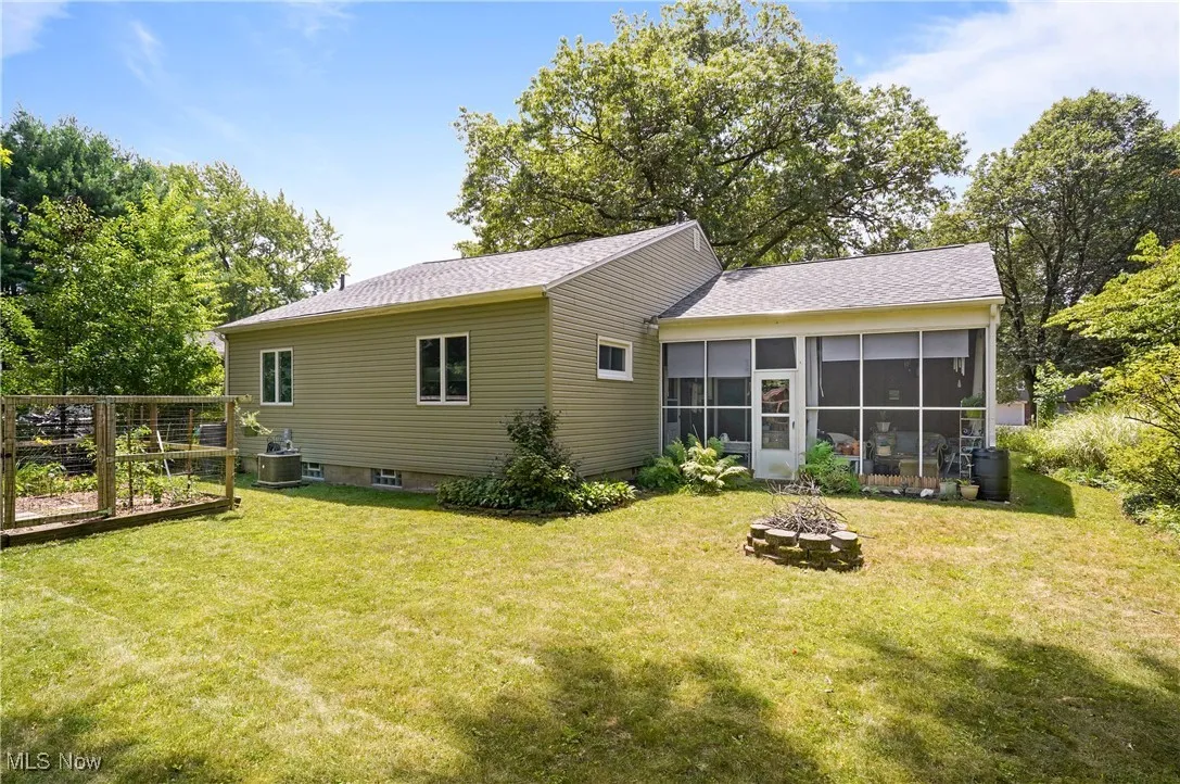 Back of house featuring a fire pit, a sunroom, a lawn, a vegetable garden, and a shingled roof