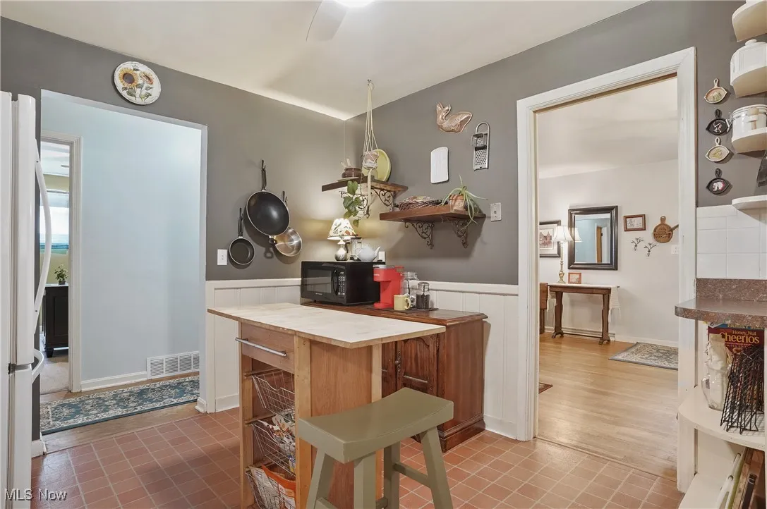 Kitchen featuring black microwave, a wainscoted wall, freestanding refrigerator, butcher block counters, and ceiling fan