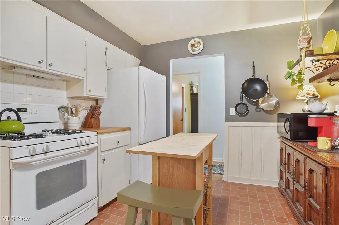 Kitchen with white range with gas cooktop, black microwave, butcher block countertops, white cabinetry, and wainscoting