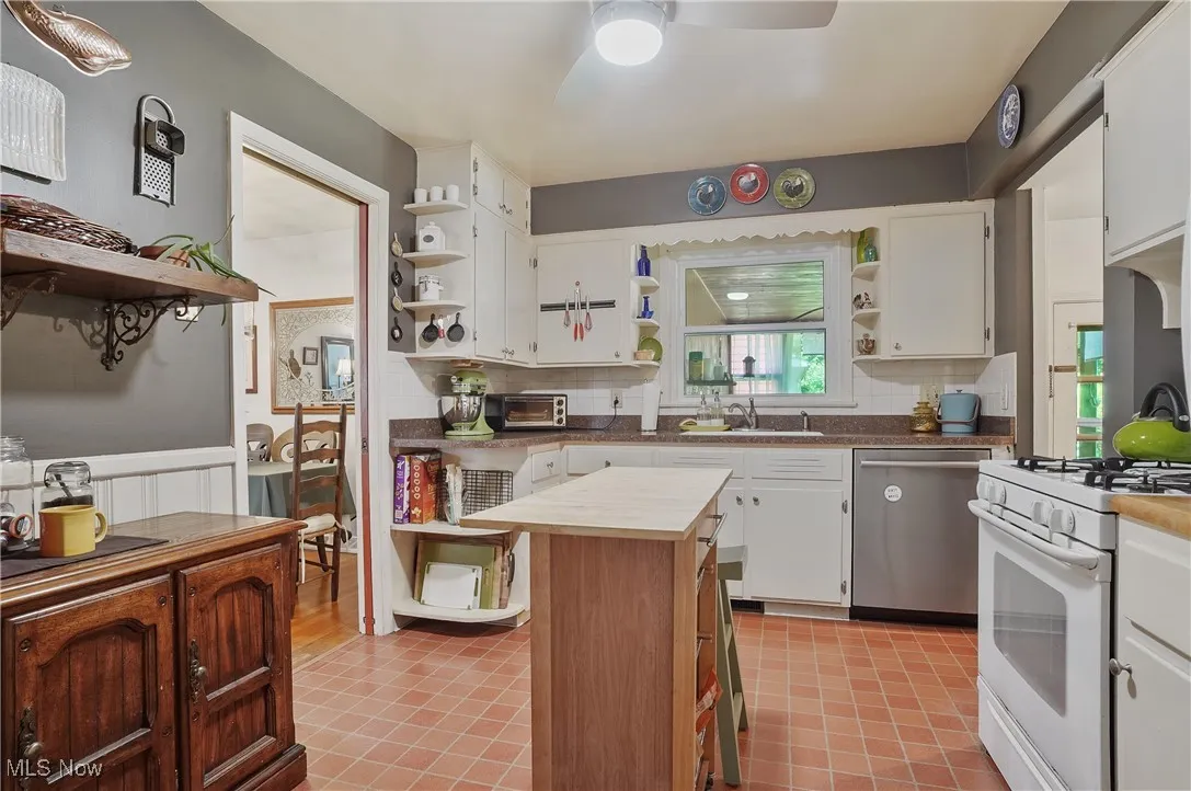 Kitchen with open shelves, dishwasher, white gas stove, ceiling fan, and wainscoting