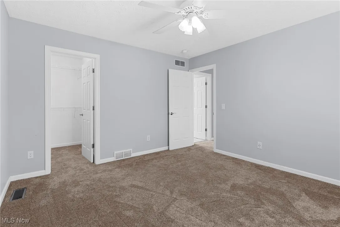 Unfurnished bedroom with carpet, a spacious closet, and ceiling fan