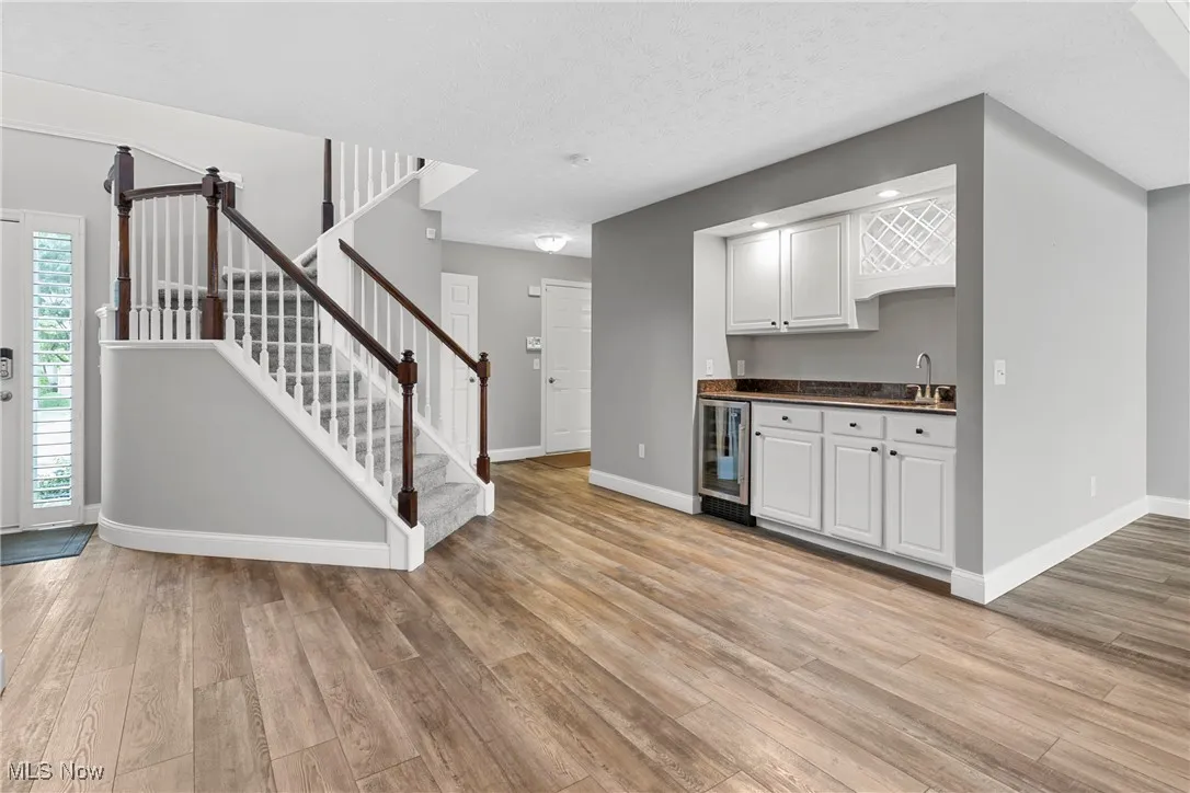 Kitchen featuring wine cooler, light wood-type flooring, white cabinets, dark countertops, and a textured ceiling