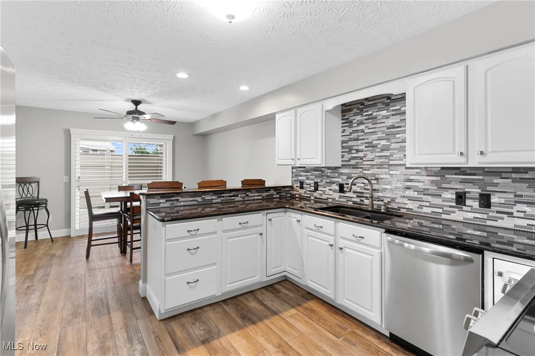 Kitchen with stainless steel dishwasher, a ceiling fan, a peninsula, a textured ceiling, and backsplash