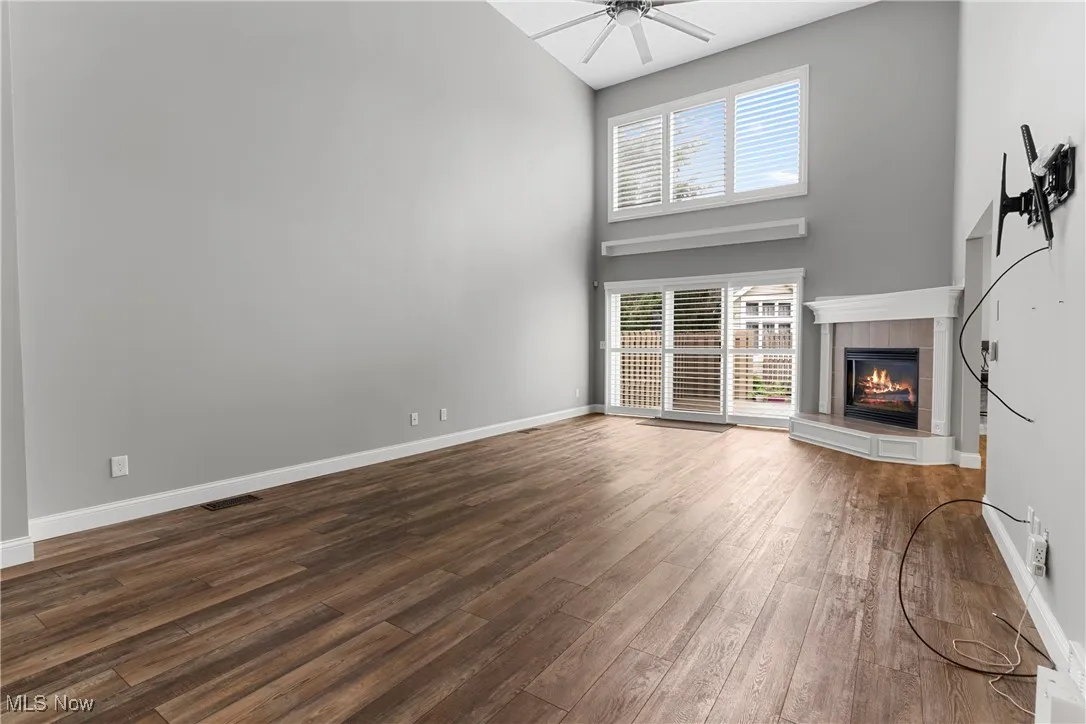 Unfurnished living room featuring high vaulted ceiling, a tile fireplace, dark wood-type flooring, a ceiling fan, and plenty of natural light