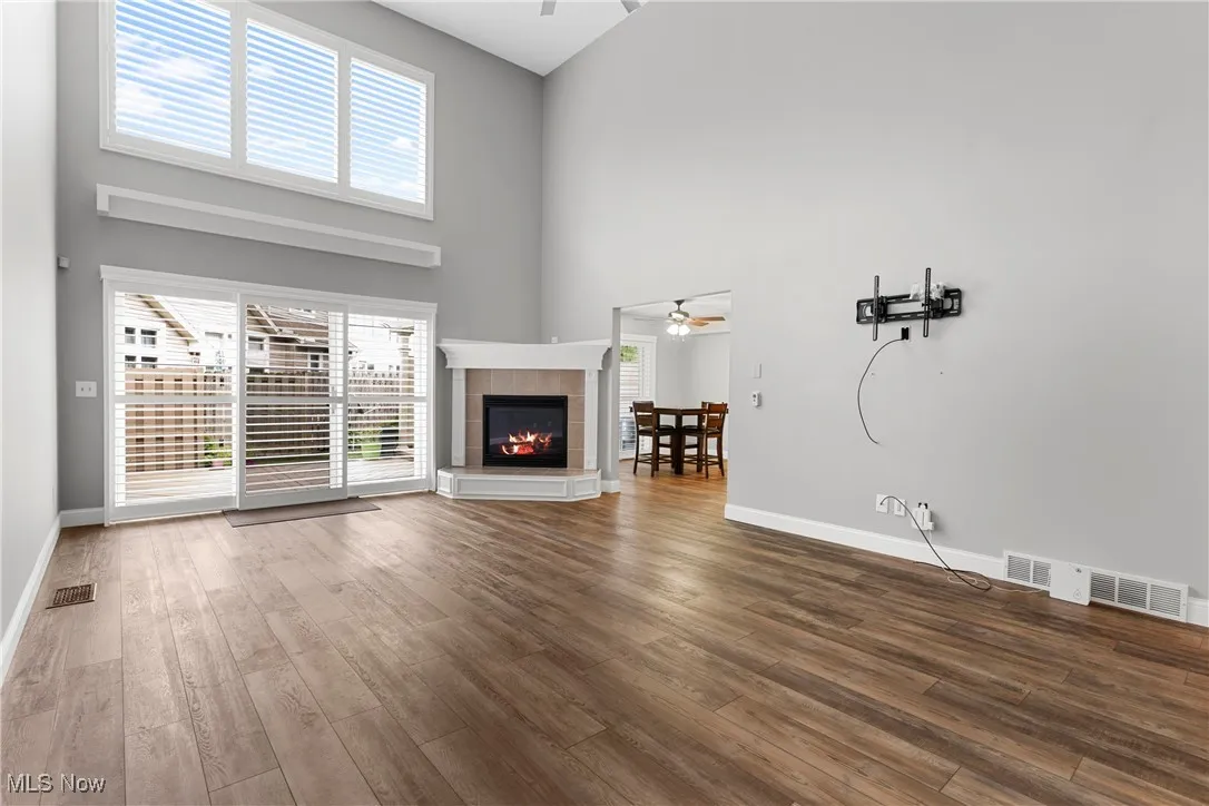 Unfurnished living room with a ceiling fan, wood finished floors, a fireplace, healthy amount of natural light, and a towering ceiling