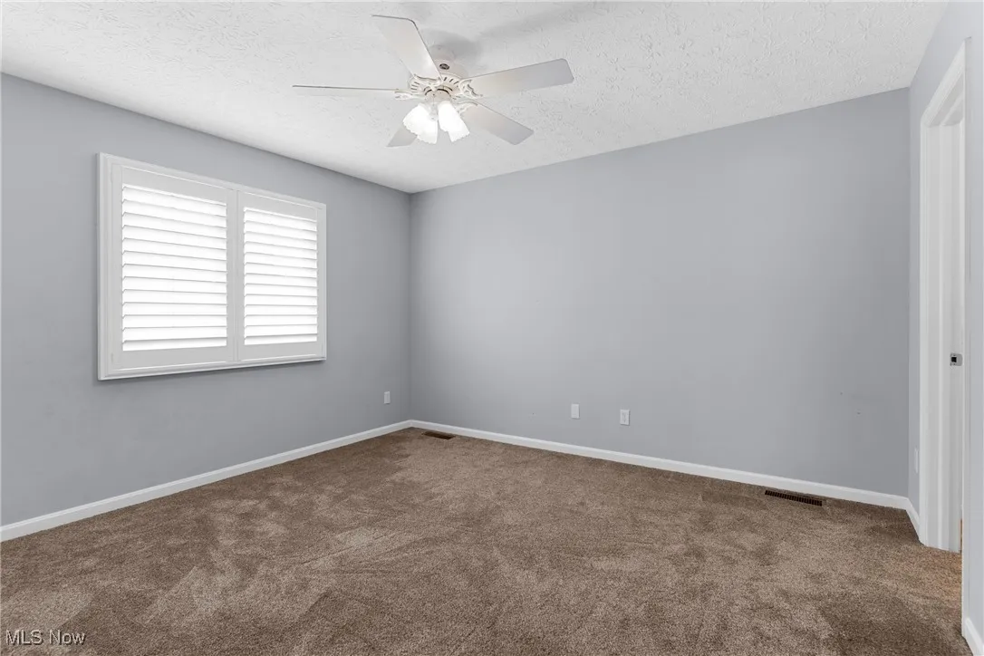 Empty room featuring carpet flooring, a ceiling fan, and a textured ceiling