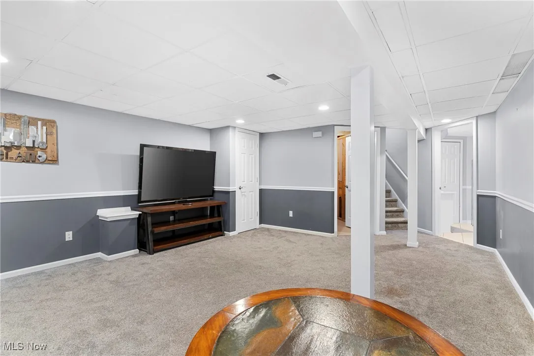Carpeted living room featuring stairs, recessed lighting, and a paneled ceiling