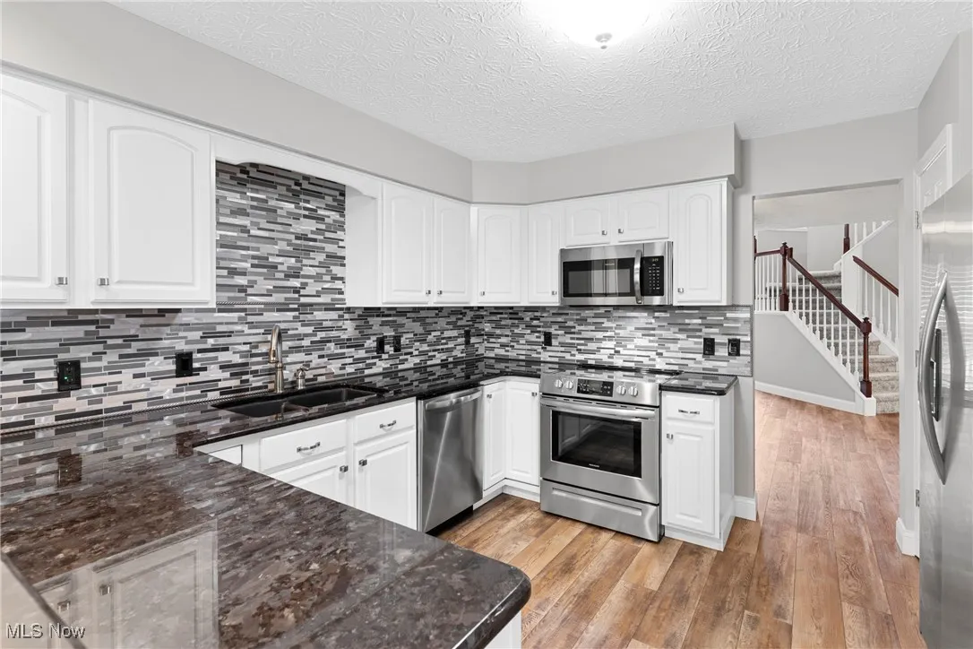 Kitchen with appliances with stainless steel finishes, light wood-style floors, white cabinetry, dark stone counters, and a textured ceiling