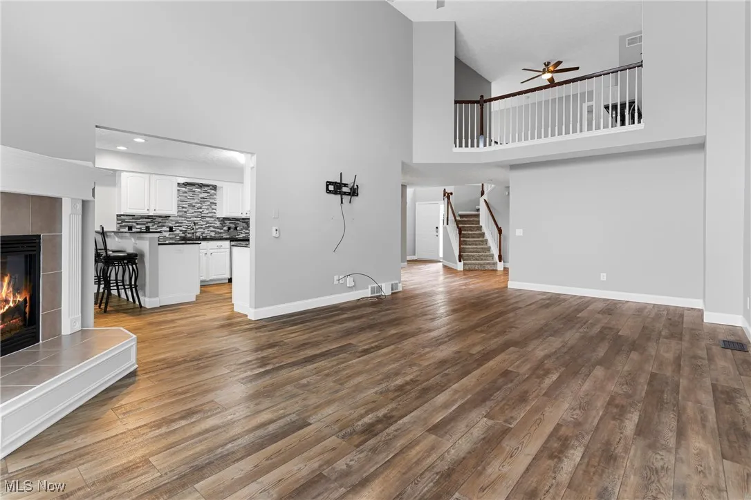 Unfurnished living room with a fireplace, a towering ceiling, ceiling fan, stairs, and wood finished floors