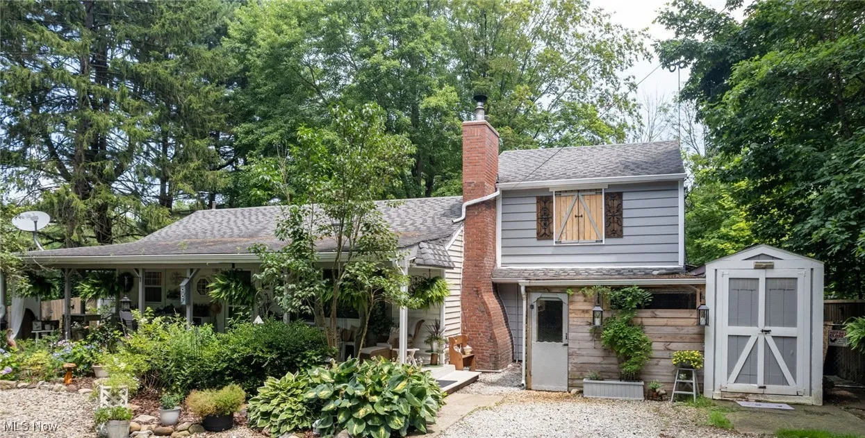 View of front of house featuring a chimney, a storage shed, and roof with shingles