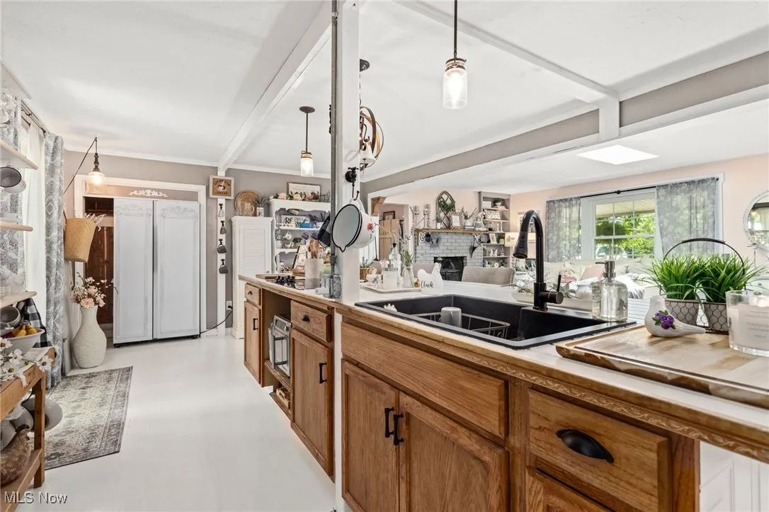 Kitchen featuring brown cabinetry, pendant lighting, beamed ceiling, paneled built in refrigerator, and light floors