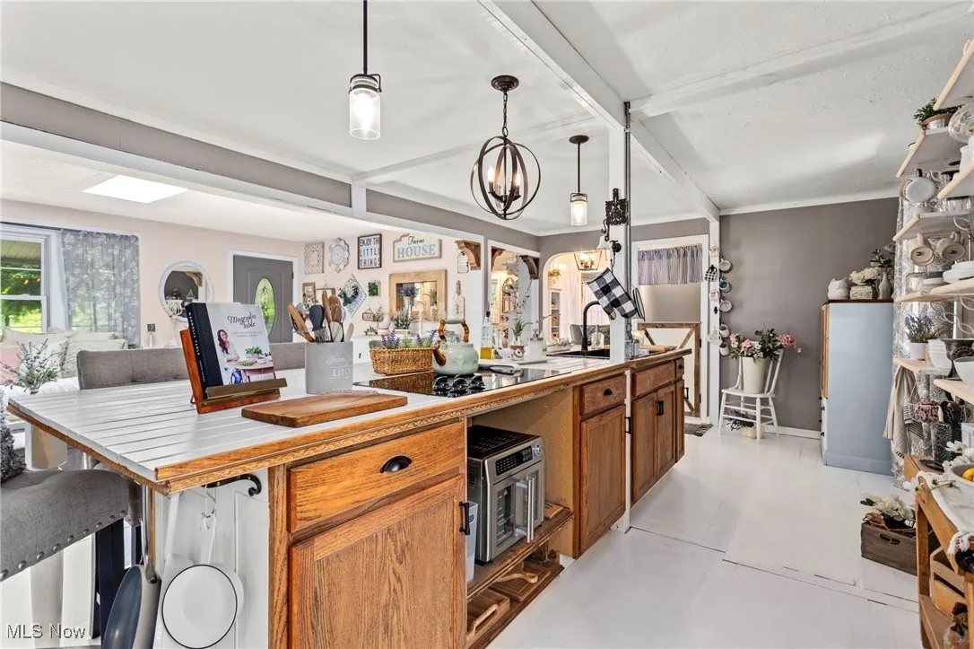 Kitchen with brown cabinetry, beamed ceiling, hanging light fixtures, a chandelier, and black electric stovetop