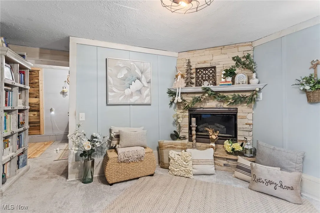 Living area featuring a stone fireplace, a textured ceiling, and carpet flooring