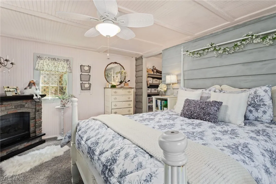 Bedroom with carpet floors, a fireplace with raised hearth, and a ceiling fan