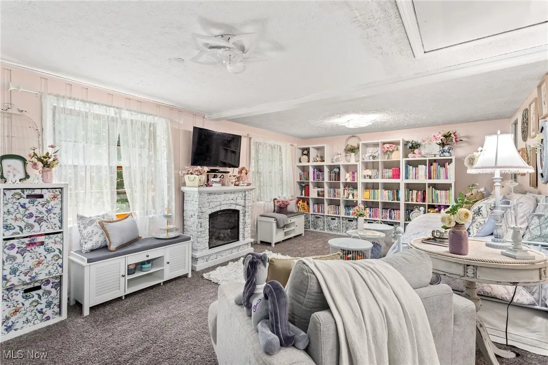 Carpeted living area featuring a textured ceiling, ceiling fan, and a stone fireplace
