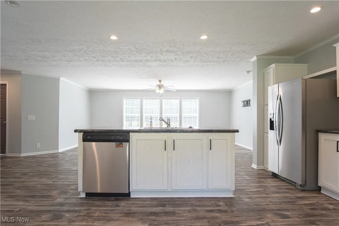 Kitchen featuring appliances with stainless steel finishes, crown molding, dark wood-style floors, a center island with sink, and a textured ceiling
