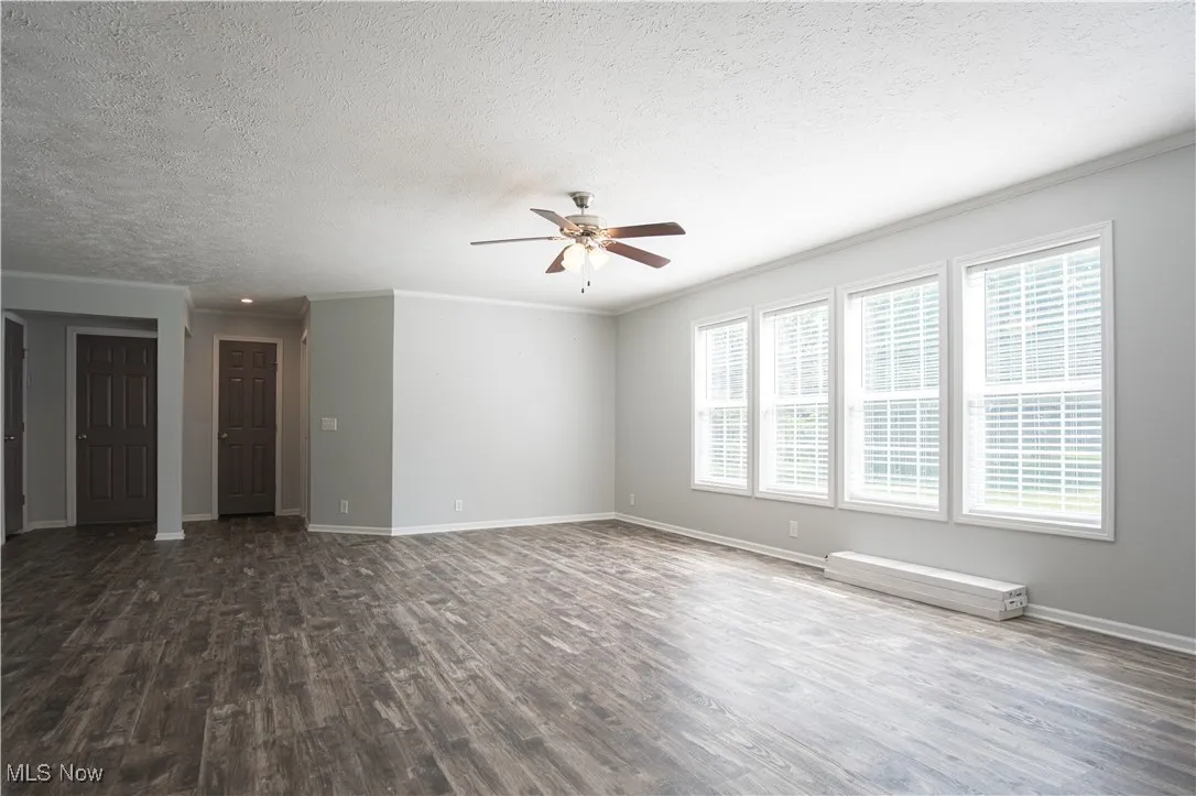 Empty room with dark wood-style floors, ceiling fan, a textured ceiling, and ornamental molding