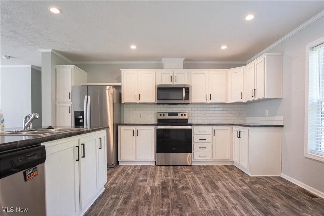 Kitchen with appliances with stainless steel finishes, dark countertops, tasteful backsplash, dark wood-type flooring, and white cabinets