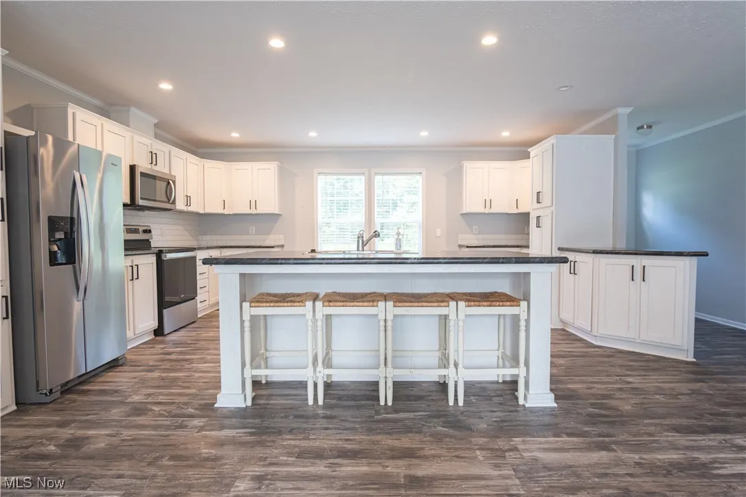 Kitchen with appliances with stainless steel finishes, crown molding, dark countertops, a breakfast bar, and white cabinets