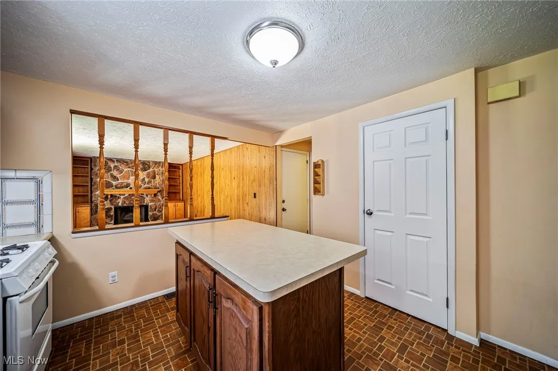 Kitchen featuring gas range gas stove, light countertops, brick patterned flooring, a kitchen island, and a textured ceiling