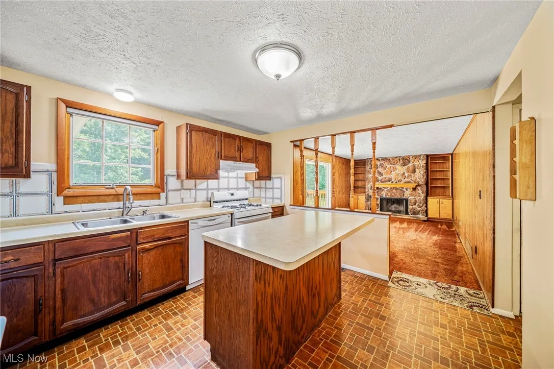 Kitchen with white appliances, plenty of natural light, a fireplace, light countertops, and a textured ceiling