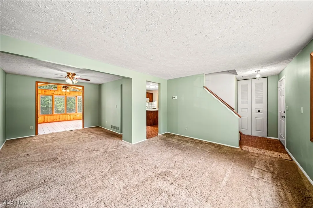 Unfurnished living room with a textured ceiling, a ceiling fan, and carpet flooring