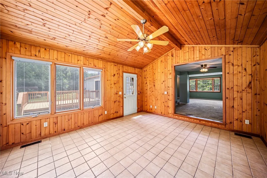 Empty room featuring wood ceiling, a ceiling fan, and wooden walls
