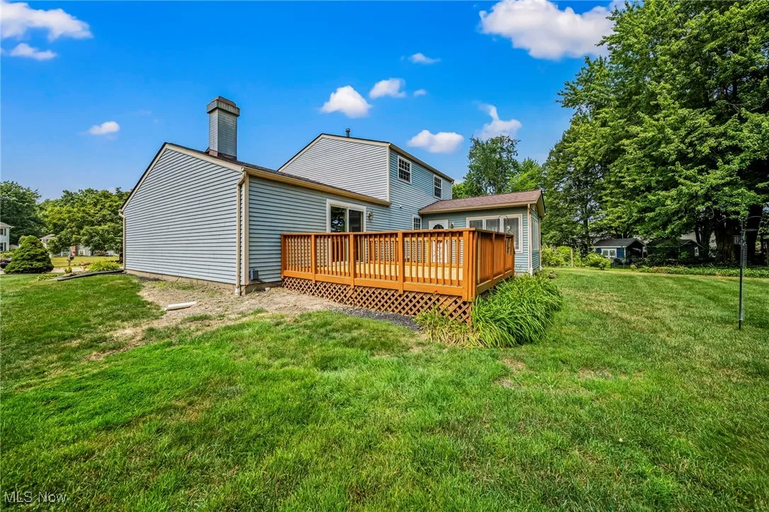 Rear view of house with a deck, a lawn, and a chimney