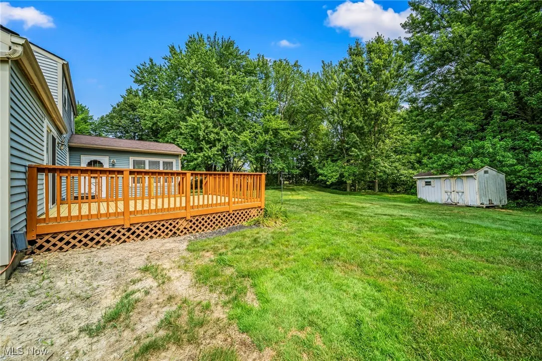 View of green lawn with a storage unit and a deck
