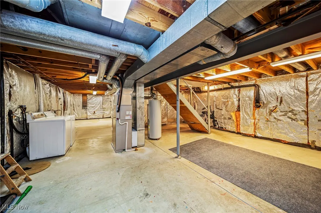 Unfinished basement with water heater, separate washer and dryer, heating unit, and stairway