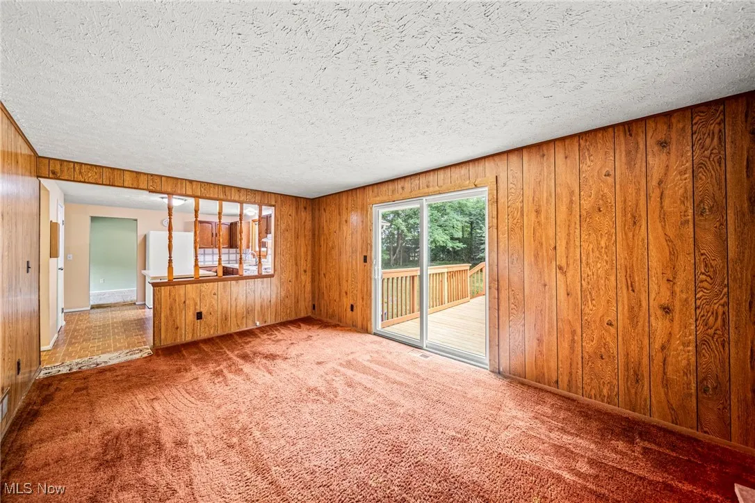 Empty room featuring a textured ceiling, carpet, and wooden walls