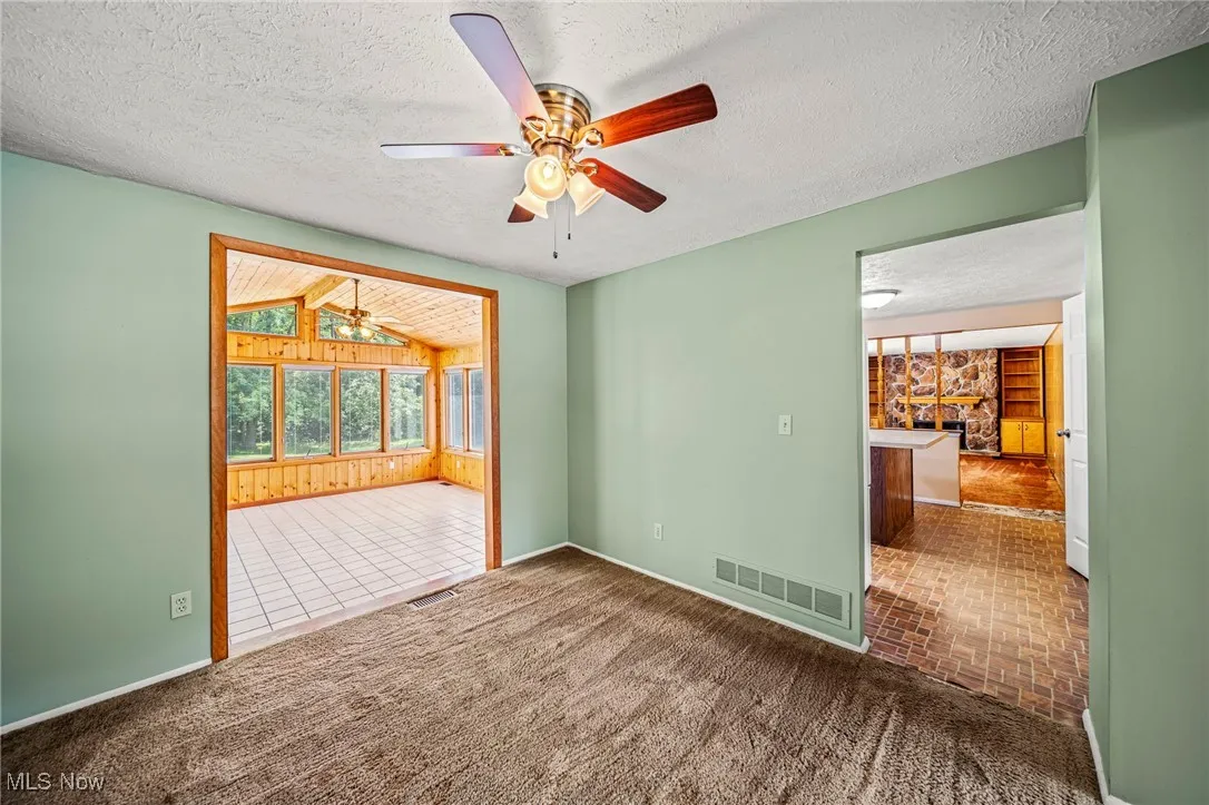 Spare room with ceiling fan, a stone fireplace, a textured ceiling, and wood walls