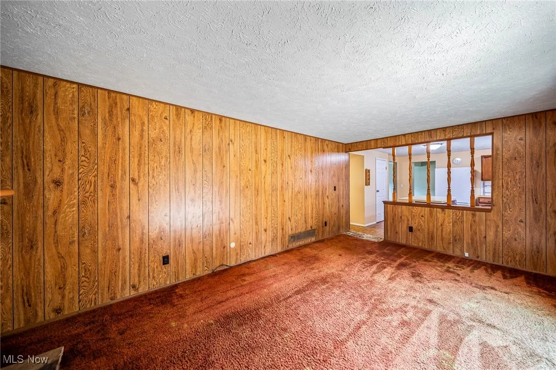 Empty room with carpet, wood walls, and a textured ceiling
