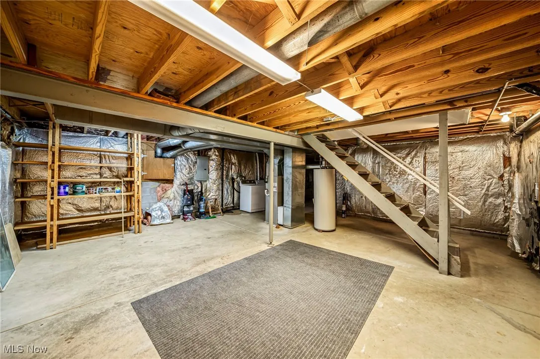 Unfinished basement with electric panel, gas water heater, stairs, and washer / dryer