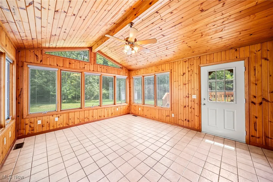 Unfurnished sunroom featuring healthy amount of natural light, wooden ceiling, wooden walls, and tile patterned floors