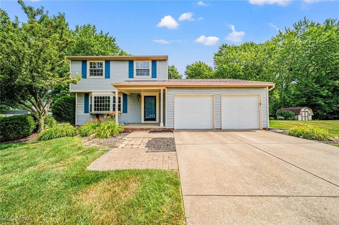 Traditional-style house featuring a garage, a storage shed, concrete driveway, a front yard, and a porch