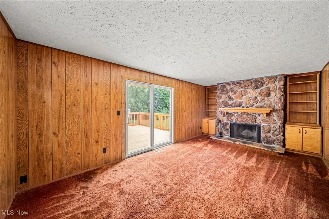 Unfurnished living room with a textured ceiling, a fireplace, wooden walls, built in features, and carpet