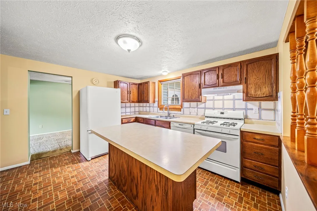 Kitchen with white appliances, under cabinet range hood, brick patterned floors, and light countertops