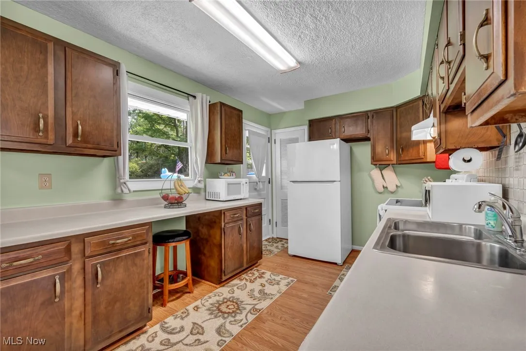 Kitchen with white appliances, a textured ceiling, light wood-type flooring, light countertops, and built in desk