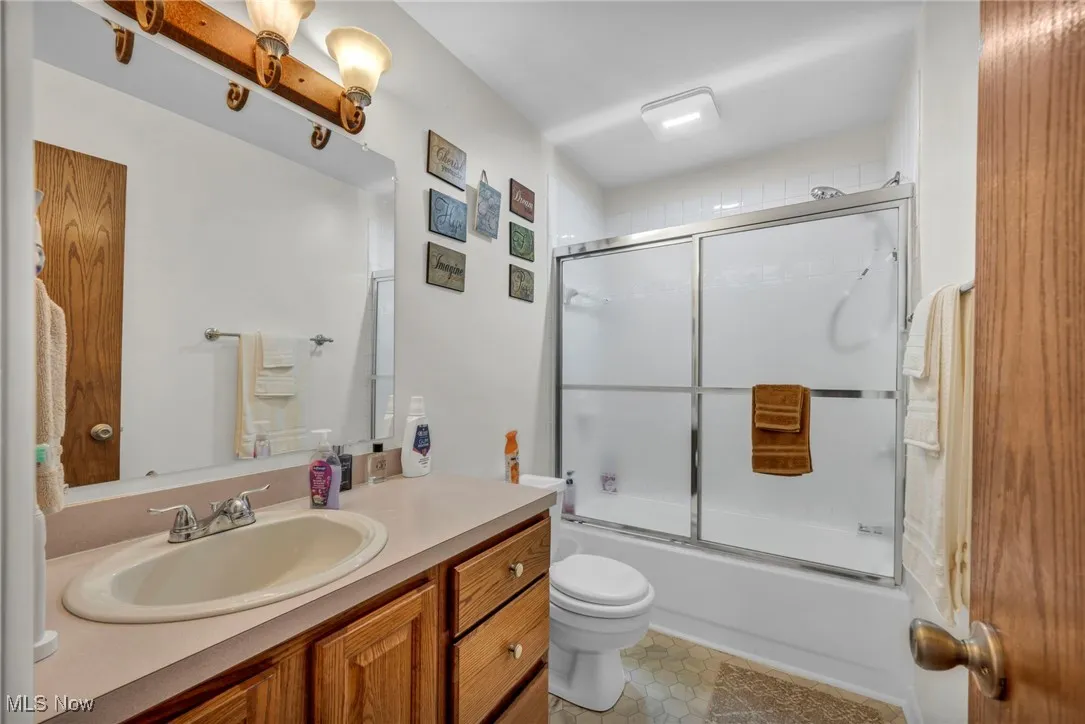 Full bath with vanity, bath / shower combo with glass door, and tile patterned floors