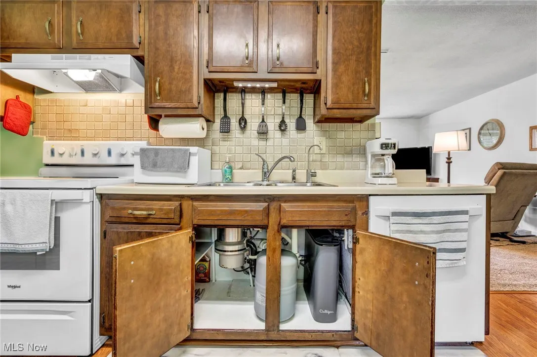 Kitchen with under cabinet range hood, white appliances, backsplash, and light countertops