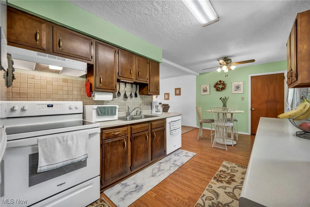 Kitchen with white appliances, under cabinet range hood, backsplash, a ceiling fan, and light wood-style flooring