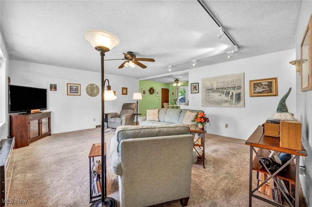 Living room with ceiling fan, carpet floors, a textured ceiling, and track lighting