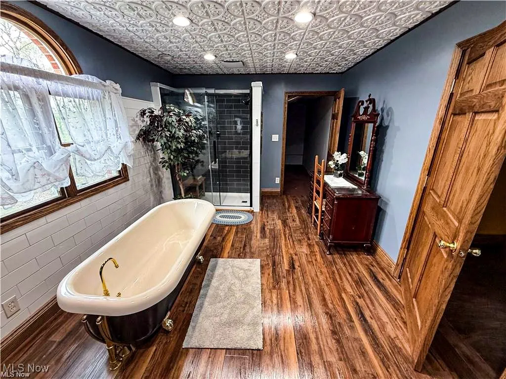 Full bath featuring an ornate ceiling, wood finished floors, tile walls, a freestanding tub, and a shower stall
