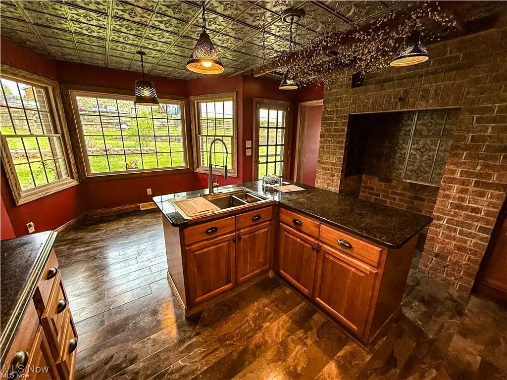 Kitchen featuring an ornate ceiling, healthy amount of natural light, an island with sink, decorative light fixtures, and dark wood-type flooring