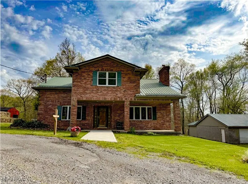 Traditional-style home featuring brick siding, a front lawn, a chimney, a metal roof, and covered porch
