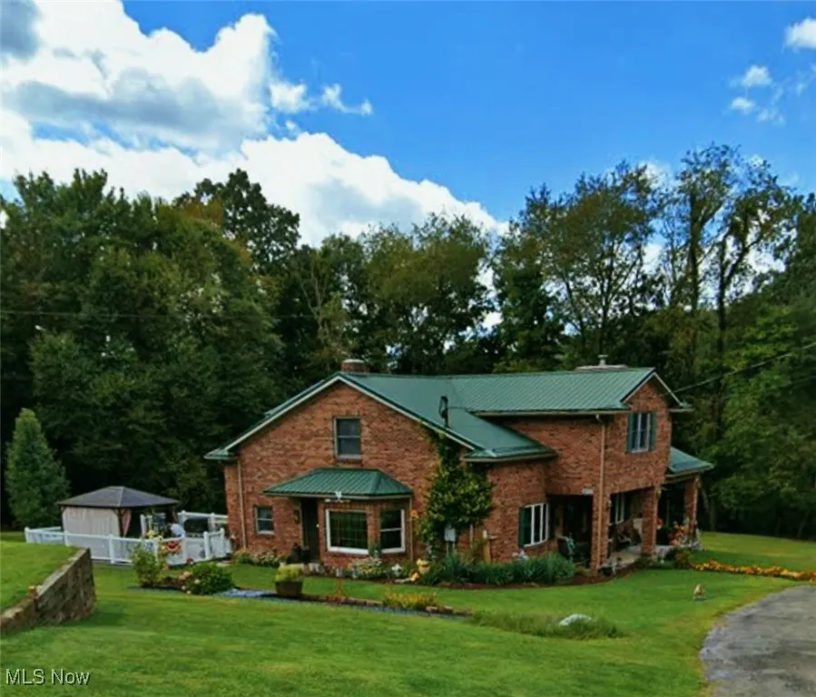 View of front facade with brick siding, a front yard, a metal roof, and a wooded view