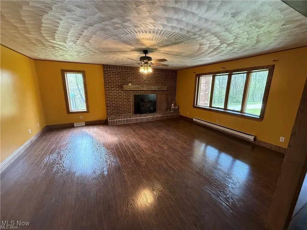 Unfurnished living room with a baseboard heating unit, a ceiling fan, healthy amount of natural light, and wood finished floors