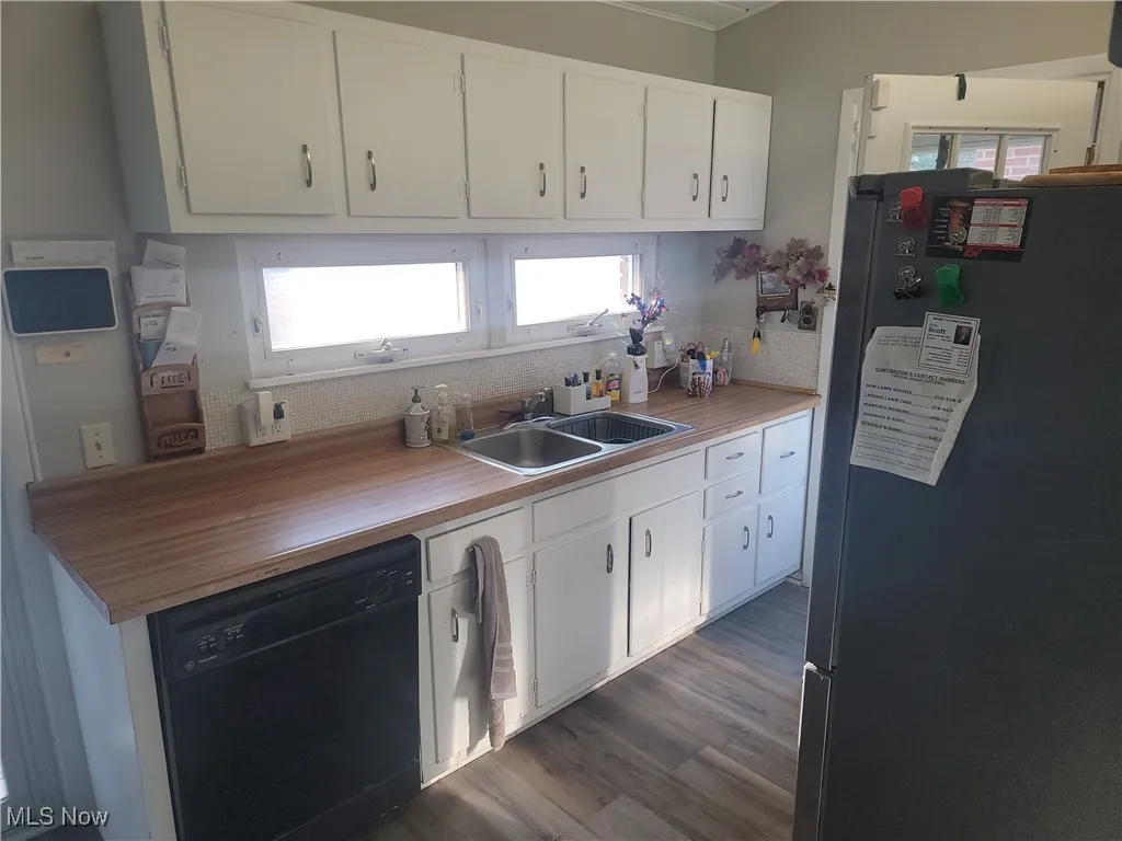 Kitchen featuring freestanding refrigerator, black dishwasher, white cabinetry, and dark wood finished floors