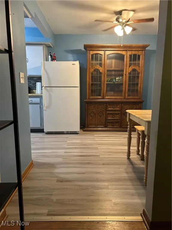 Kitchen featuring fridge, ceiling fan, light wood-type flooring, and glass insert cabinets